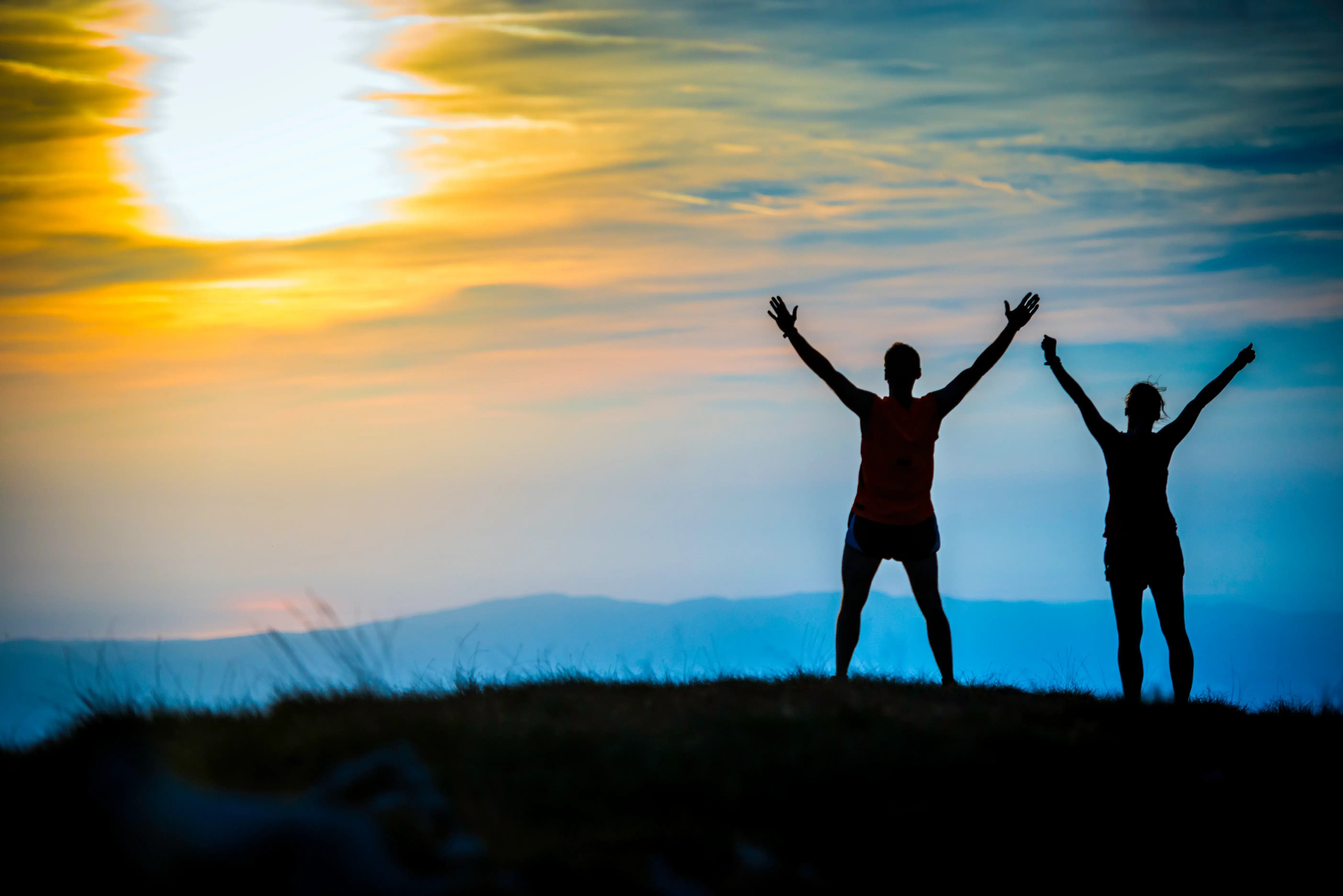 Two people with arms raised against a sunset sky